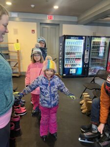 picture of 3 smiling children in a row in winter coats, hats, and ice skates.