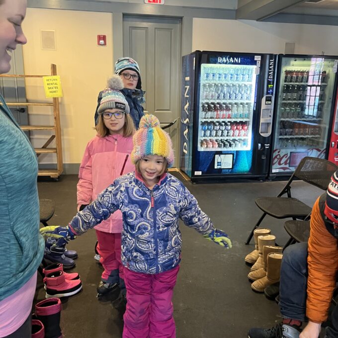 picture of 3 smiling children in a row in winter coats, hats, and ice skates.