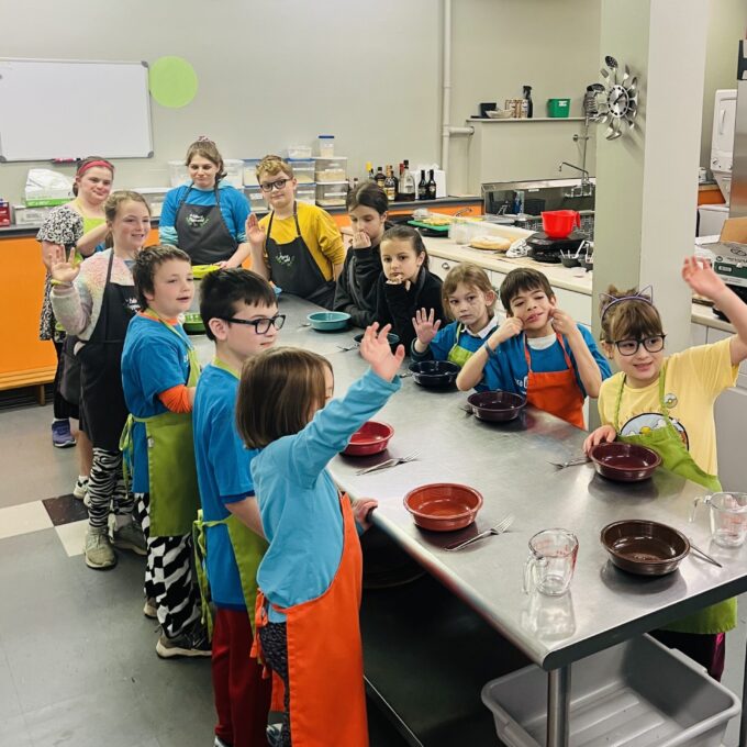 picture of 12 children around a countertop smiling and raising their hands.