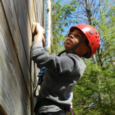 boy wearing red hard hat climbing wooden wall